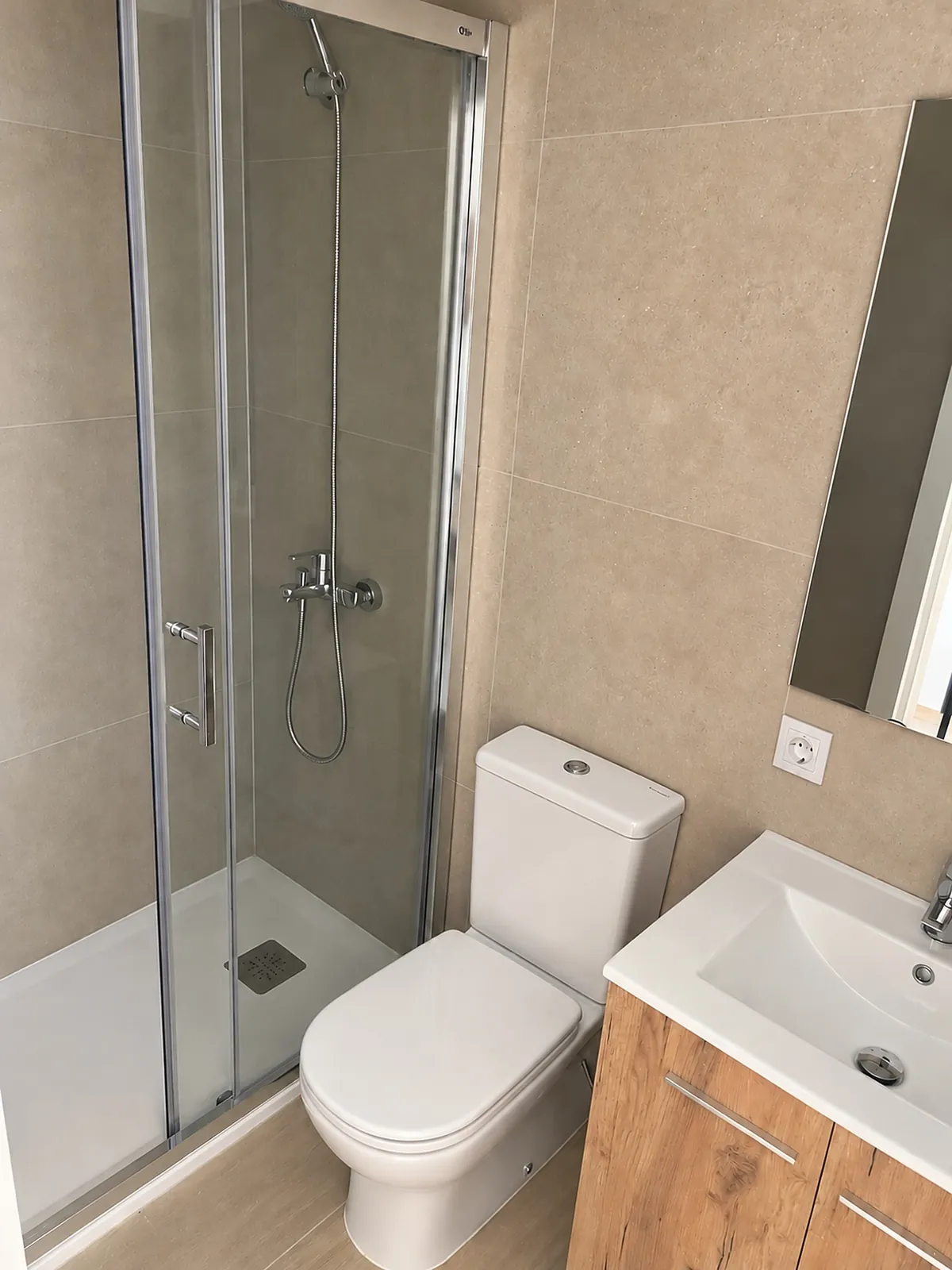 Baño con plato de ducha, mampara, inodoro y mueble de lavabo.